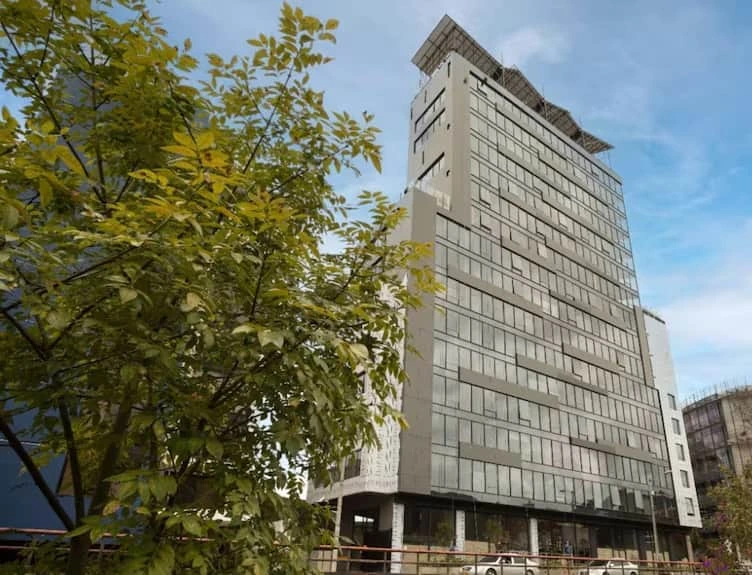 Torre acristalada entre árboles asociada a la experiencia con Constructora Orbimundo